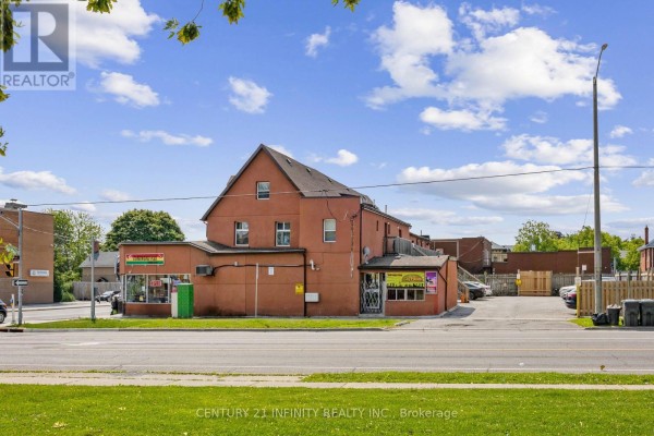 Side and rear exterior of a commercial building showing storefronts, parking lot, and green space. - 134-142 Simcoe Street S, Oshawa