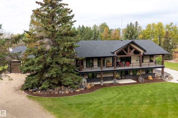 Front of a large house with a covered deck, stone accents, and a manicured lawn. - #134 54500 Lac Ste Anne, Rural Sturgeon County