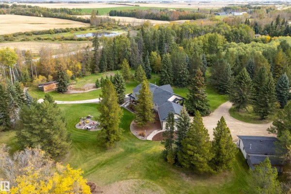 Aerial view of a house nestled among trees with a fire pit area and a pond in the distance. - #134 54500 Lac Ste Anne, Rural Sturgeon County