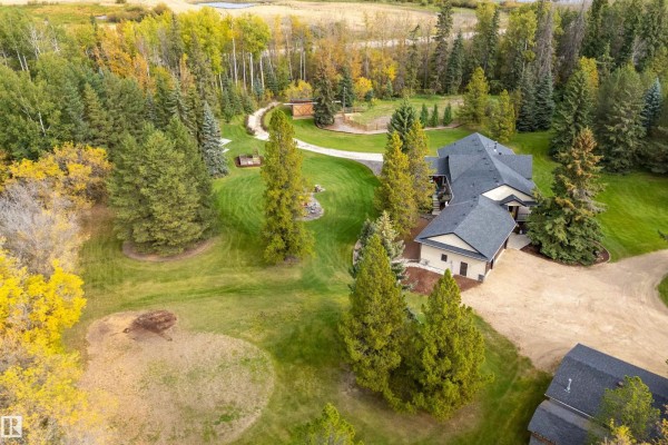 Aerial view of a house with a garage and surrounding trees, fields, and distant hills. - #134 54500 Lac Ste Anne, Rural Sturgeon County