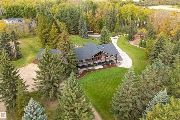 Aerial view of a large house with a dark roof, a wrap-around deck, and abundant surrounding forest. - #134 54500 Lac Ste Anne, Rural Sturgeon County