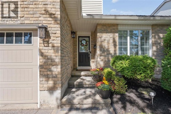 Front entrance of a house with a black front door, stone steps, and surrounding greenery. - 134 Bechtel Drive, Kitchener