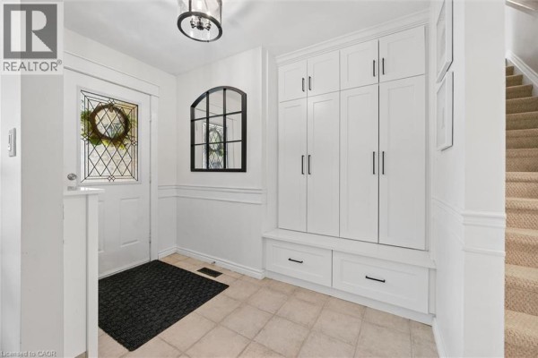 Bright entryway with a white built-in storage bench and cabinets, a tiled floor, and carpeted stairs. - 134 Bechtel Drive, Kitchener