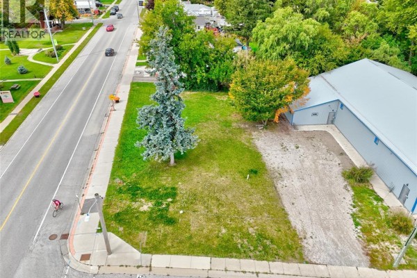 Aerial view of a grassy corner lot with a mature tree and adjacent industrial building. - 134 County Rd 34 W., Cottam