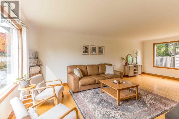 Living room with a brown leather sofa, two cream armchairs, a wooden coffee table, and a patterned rug. - 134 Florwin Dr, Sault Ste  Marie