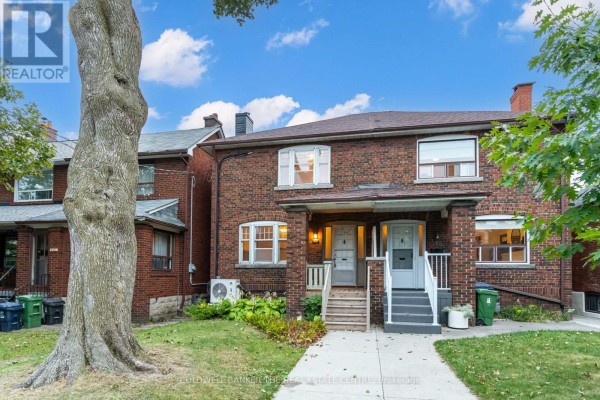 Exterior of a red brick duplex with mature tree in front yard. - 134 Harvie Avenue, Toronto