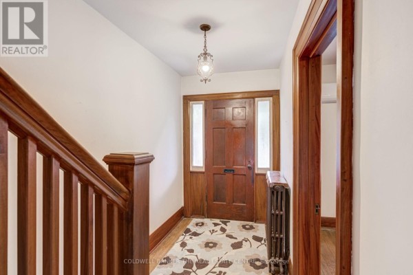 Interior entryway with dark wood trim, staircase, patterned rug, and radiator. - 134 Harvie Avenue, Toronto