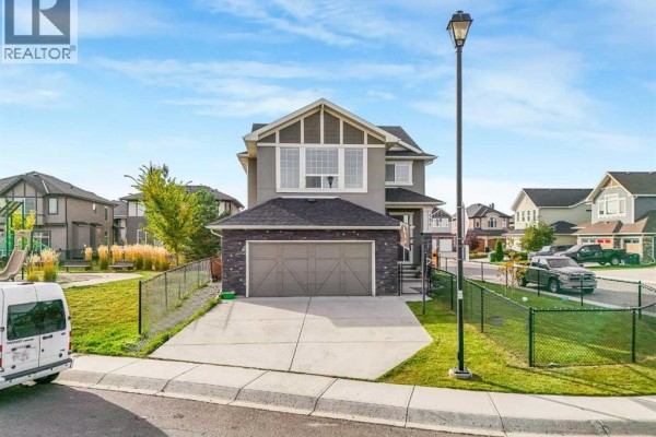 Front exterior of a two-story house with a stone accent garage door and lawn. - 134 Kinniburgh Lane, Chestermere