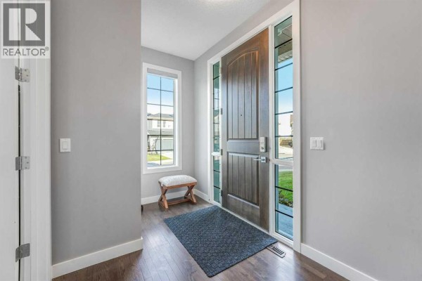 Interior foyer with a large wooden front door, glass panels, and wood floors. - 134 Kinniburgh Lane, Chestermere