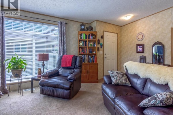 Living room featuring a recliner, bookshelf, and large windows - 1340 Hwy 3a Highway Unit# 13, Keremeos