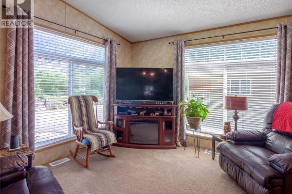 Cozy living area with TV, armchair, and natural light from windows - 1340 Hwy 3a Highway Unit# 13, Keremeos