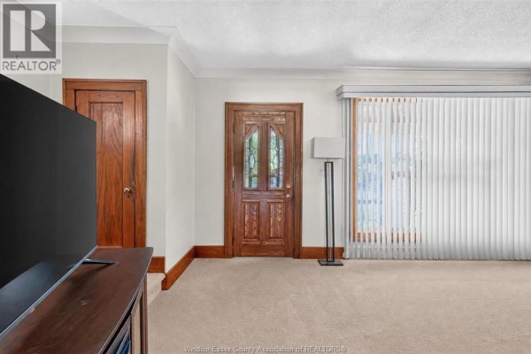 Living room interior with a large window, vertical blinds, two wooden doors, and a television. - 1342 Hall Avenue, Windsor