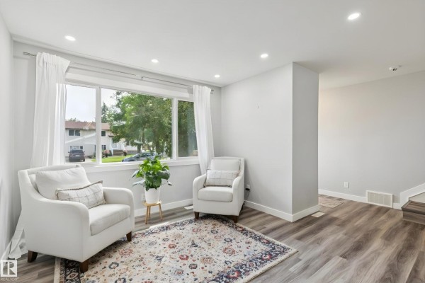 Living area with two white armchairs, a patterned rug, and a large window overlooking the street. - 13428 117a Av Nw, Edmonton