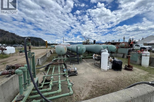 Yard with green pipes and pumps, various propane tanks, and vehicles under cloudy sky. - 1345 Cardy Drive, Scotch Creek