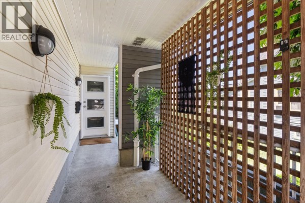 Walkway leading to townhouse entrance with white siding, hanging plants, and a wooden privacy screen. - 1345 Woodland Drive, Vancouver