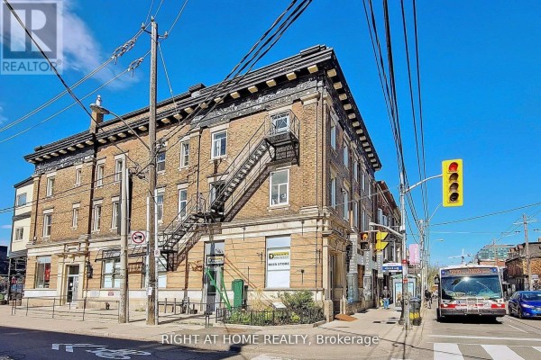 Three-story brick building with fire escape stairs visible from the street with traffic. - 1346 Queen Street W, Toronto