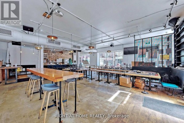 Large open-concept commercial space with long wooden tables, stools, and industrial lighting. - 1346 Queen Street W, Toronto