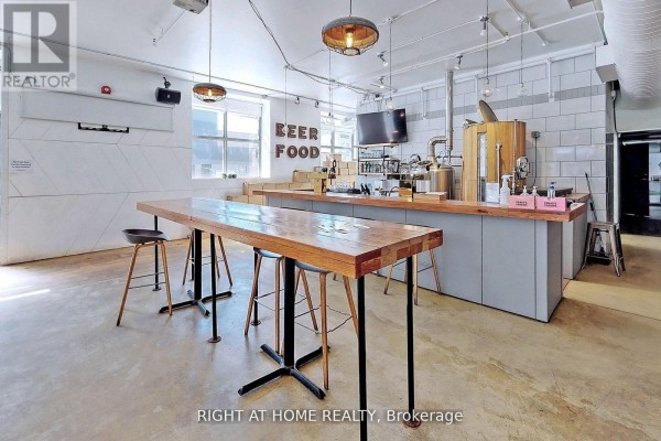Commercial space with a long wooden table, stools, and a bar area with brewing equipment. - 1346 Queen Street W, Toronto