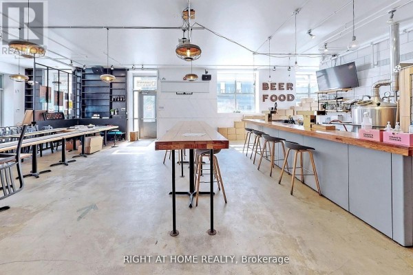 Wide view of a commercial space with tables, bar, brewing equipment, and shelving. - 1346 Queen Street W, Toronto