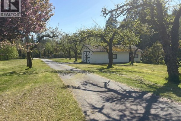 View of a paved driveway leading past a white detached garage, surrounded by a lawn and numerous mature trees. - 1346 Russell Road, Gibsons