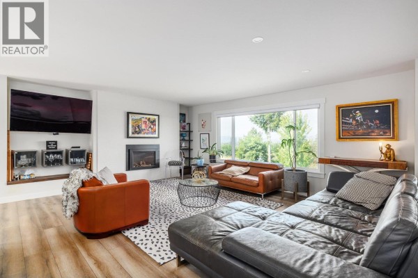 Living room with a fireplace, leather sofas, chairs, and a large window overlooking the landscape. - 13487 Middle Bench Road, Lake Country