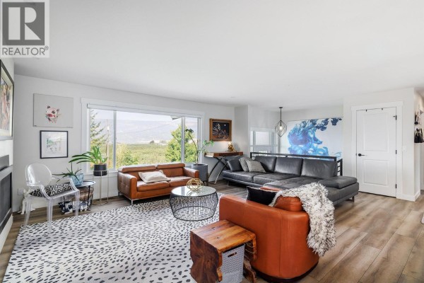 Spacious living room featuring leather sectional, accent chairs, coffee table, and large windows with a view. - 13487 Middle Bench Road, Lake Country