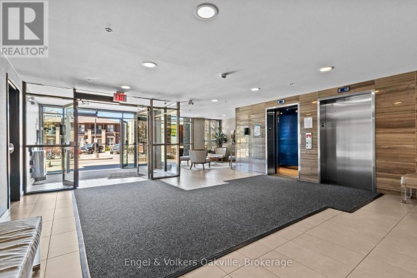 Apartment building lobby with glass doors, elevators, seating area, and tiled floors. - 135 - 5010 Corporate Drive, Burlington
