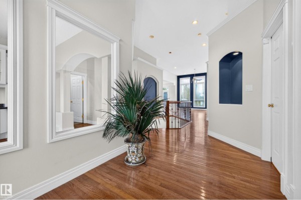 Interior hallway with hardwood floors, large mirror, potted plant, and view of the staircase and living area. - #135 52304 Rge Road 233, Rural Strathcona County