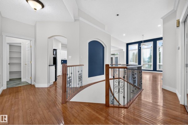 Interior hallway with hardwood floors, staircase, pantry door, and view of the living room with large windows. - #135 52304 Rge Road 233, Rural Strathcona County