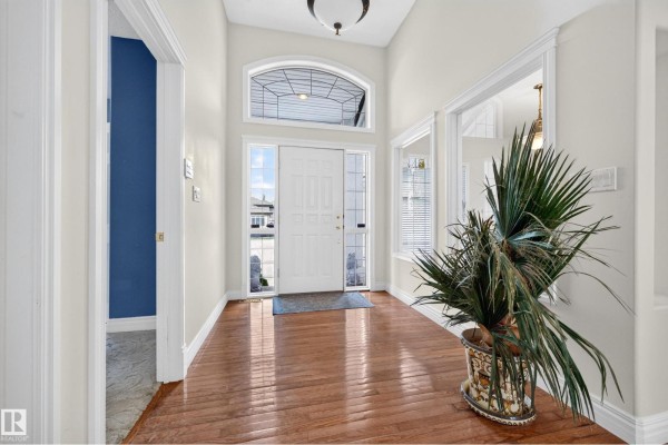 Interior foyer with white front door, arched transom window, hardwood floors, and potted plant. - #135 52304 Rge Road 233, Rural Strathcona County