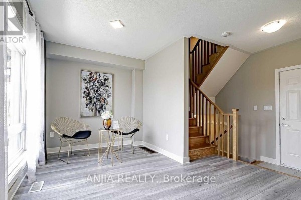 Living area with light grey wood-look flooring, beige walls, a staircase, and two chairs. - 135 Carpaccio Avenue, Vaughan