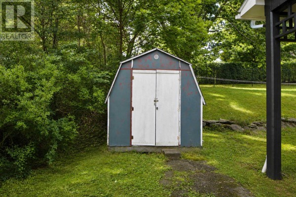 Blue storage shed with white double doors situated on a green lawn. - 135 Chelsea Court, New Glasgow