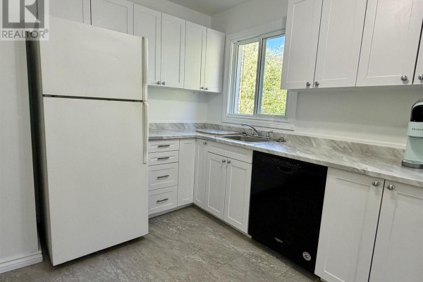 Corner view of a kitchen with white cabinets, grey countertops, sink, dishwasher, and window. - 135 Dieppe Ave, Elliot Lake
