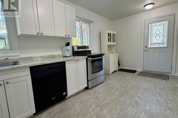 Kitchen facing the exterior door, featuring white cabinets, appliances, and grey flooring. - 135 Dieppe Ave, Elliot Lake
