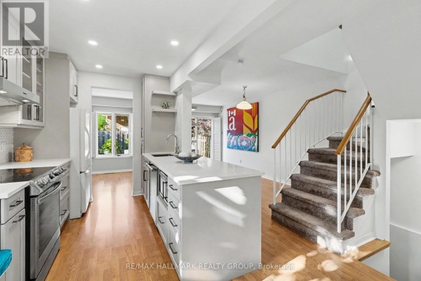 Open-concept kitchen and living area with a carpeted staircase and hardwood floors. - 135 Evelyn Avenue, Ottawa