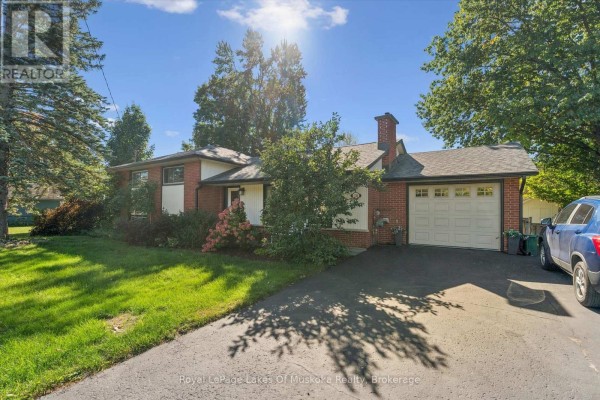 Side view of a single-story house with a brick facade, white siding, and an attached garage on a paved driveway. - 135 Muskoka Beach Road, Gravenhurst)