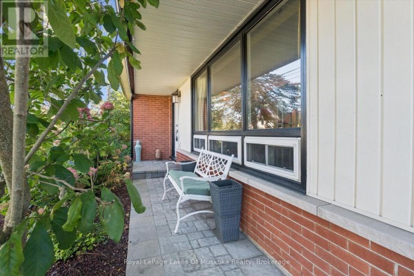 A covered front porch with a stone walkway, brick accents, and a white metal bench overlooking the garden. - 135 Muskoka Beach Road, Gravenhurst)