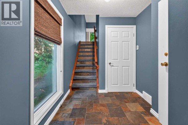 Interior foyer with slate tile floor, blue walls, and staircase. - 135 Point Drive Nw, Calgary