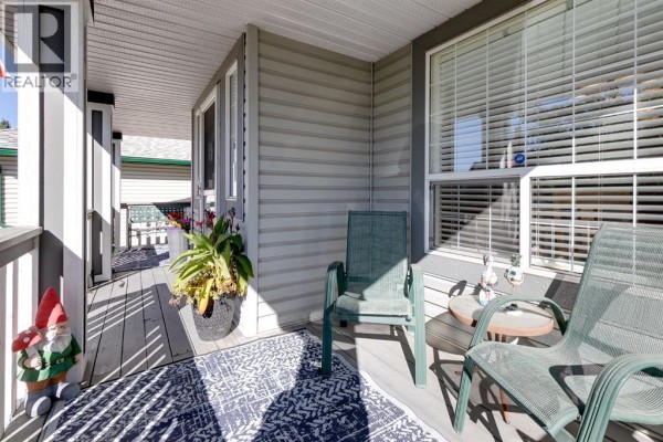 A covered porch with grey siding, featuring green chairs, a small table, and decorative garden gnomes. - 135 Springs Crescent, Airdrie