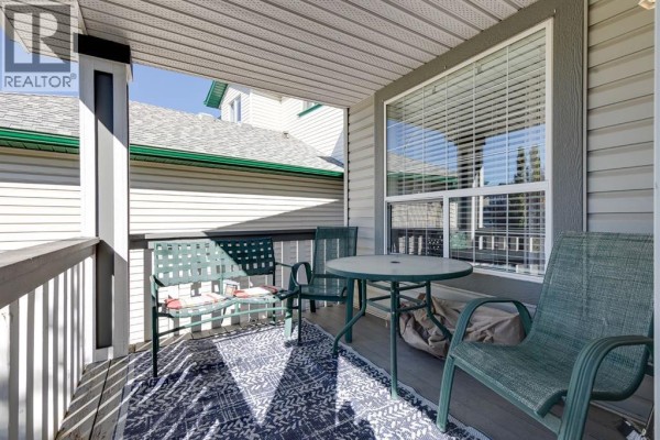 A covered porch with outdoor seating, including green chairs and a round metal table on a patterned rug. - 135 Springs Crescent, Airdrie