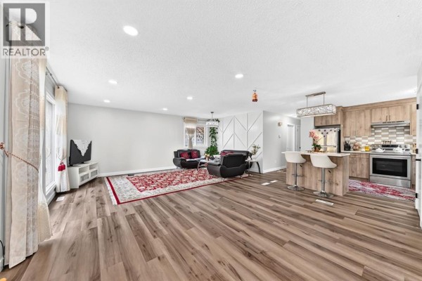 Open-concept living and kitchen area with a large red rug, black leather furniture, and light wood cabinets. - 135 Whiteview Close Ne, Calgary