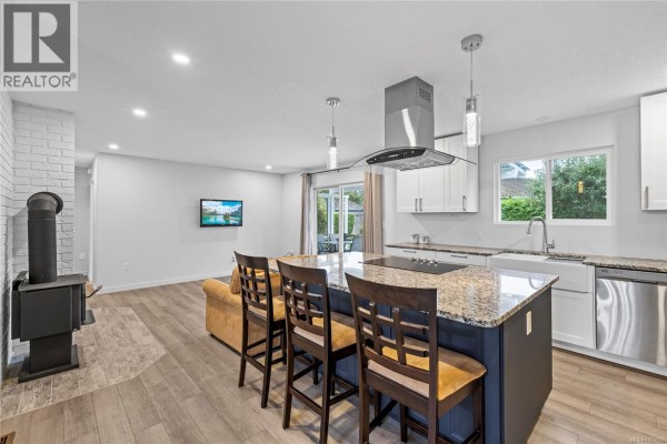 Open-concept kitchen and living space with a wood-burning stove, island, and view of the backyard. - 1350 Greenwood Way, French Creek