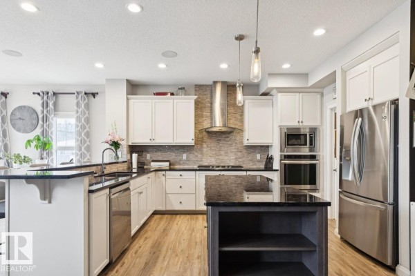 Spacious kitchen featuring white cabinetry, stone tile backsplash, and stainless steel appliances. - 1351 Secord Landing Ld Nw, Edmonton