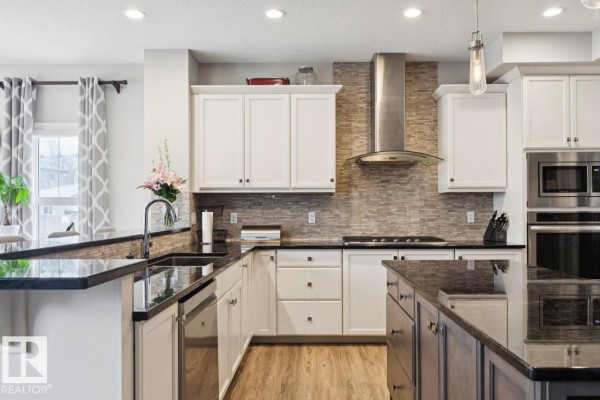 Kitchen view showing white cabinets, black granite countertops, a stainless steel range hood, and island. - 1351 Secord Landing Ld Nw, Edmonton