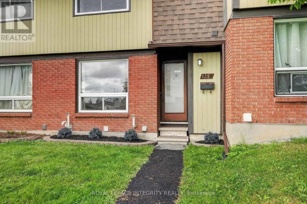 Close-up of the townhouse entrance at 135 Bakker Court, featuring red brick and pale green siding. - 1352 Bakker Court, Ottawa