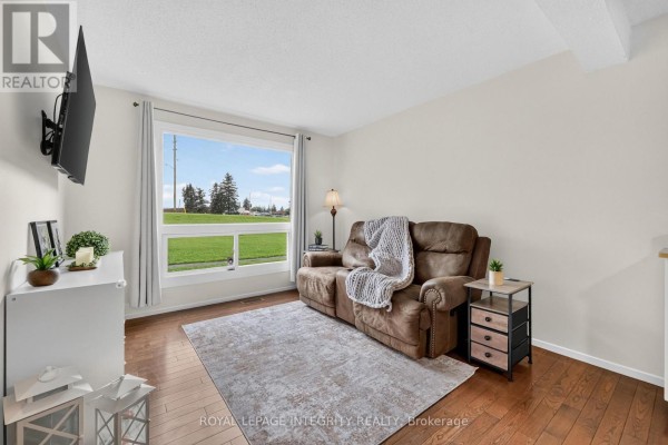 Living room with a brown recliner sofa, large window with green field view, and hardwood floors. - 1352 Bakker Court, Ottawa