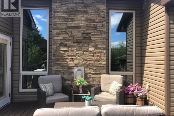 Outdoor seating area on a deck with stone accent wall and large windows. - 13520 Township Road 744, Joussard