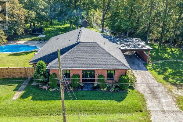 Aerial view of a red brick bungalow with a grey roof, a carport, and a swimming pool in the backyard. - 1355 Woodburn Road, Hamilton
