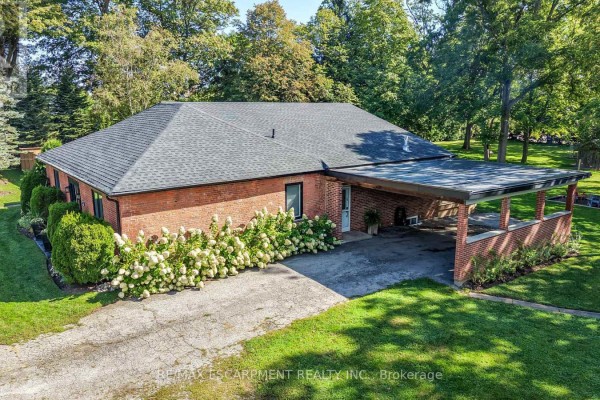 Front exterior of a red brick bungalow with a grey roof, a covered carport, and manicured landscaping. - 1355 Woodburn Road, Hamilton