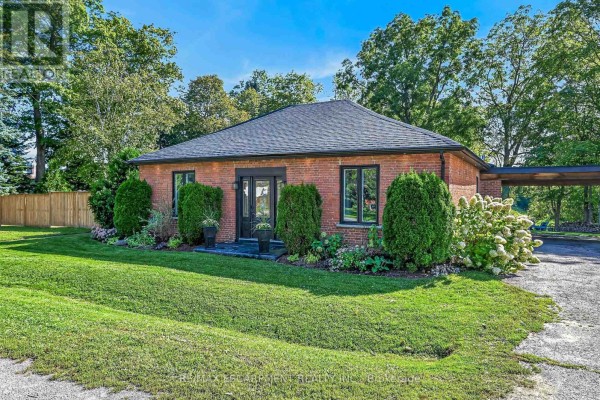 Front view of a red brick bungalow with a grey roof, black framed windows, and a covered carport. - 1355 Woodburn Road, Hamilton